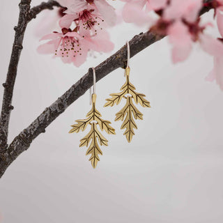 Bronze leaf-shaped earrings hanging from a branch with pink cherry blossoms.