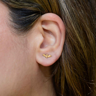 Close-up of an ear wearing a bronze bat earring with hair partially covering the frame.