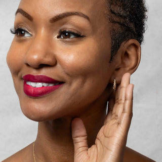 Woman with red lipstick and bronze Twisted Teardrop Huggie Hoops against a neutral background