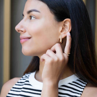 Woman adjusting her Bronze Large Teardrop Huggie Hoops with a blurred background
