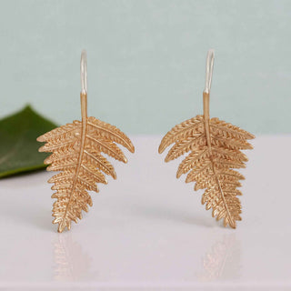 Gold leaf-shaped earrings on a light background