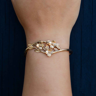 Bronze bracelet with dogwood design on a wrist against a dark background