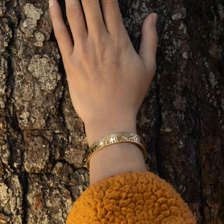 Hand with a bronze bracelet on a tree trunk
