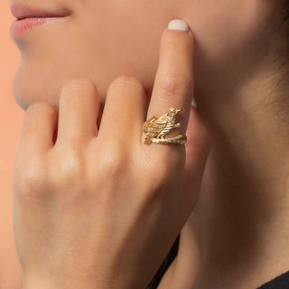 A close-up lifestyle shot of a model wearing a gold raven perched on a branch.