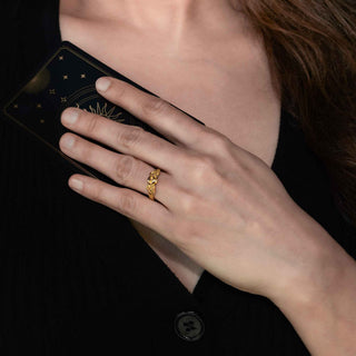 Hand wearing a gold ring holding a black tarot card against a dark background