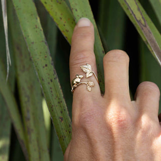 Hand wearing a gold leaf ring with green leaves in the background