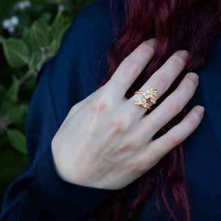 Hand wearing a gold ring with floral design against a blurred natural background