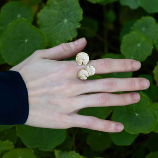 Hand wearing bronze floral ring with green leaves in the background