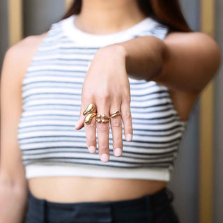 Person wearing multiple gold tone bronze rings on a blurred background
