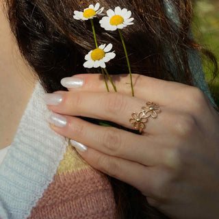 Hand wearing a bronze flower ring with three daisies in hair