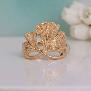 Gold leaf-shaped ring on a reflective surface with a blurred background