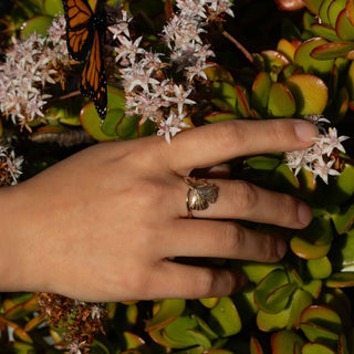 Hand with a ring on a leafy background with flowers and a butterfly.