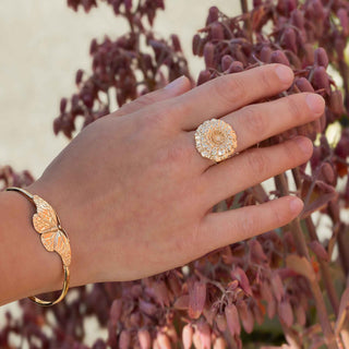 Hand wearing a bronze ring and bracelet against a blurred natural background
