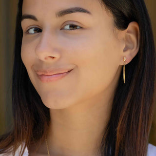 Close-up of a woman wearing Bronze Small Oval Post Earrings with Long Pod Dangle with a neutral background