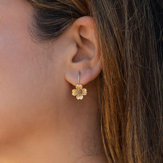 Close-up of a person wearing a gold flower-shaped earring.