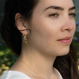 Close-up of a woman wearing  bronze earrings and a necklace with a blurred natural background