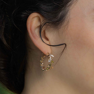 Close-up of an ear wearing a bronze hoop earring with leaf details.