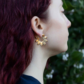 Close-up of a person wearing bronze hoop earrings with a blurred green background