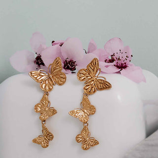 bronze butterfly earrings on a mannequin with pink flowers in the background