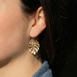 Close-up of a person wearing gold leaf-shaped earrings.