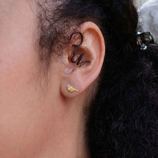 A close-up of a person's ear wearing a small bronze bird earrings